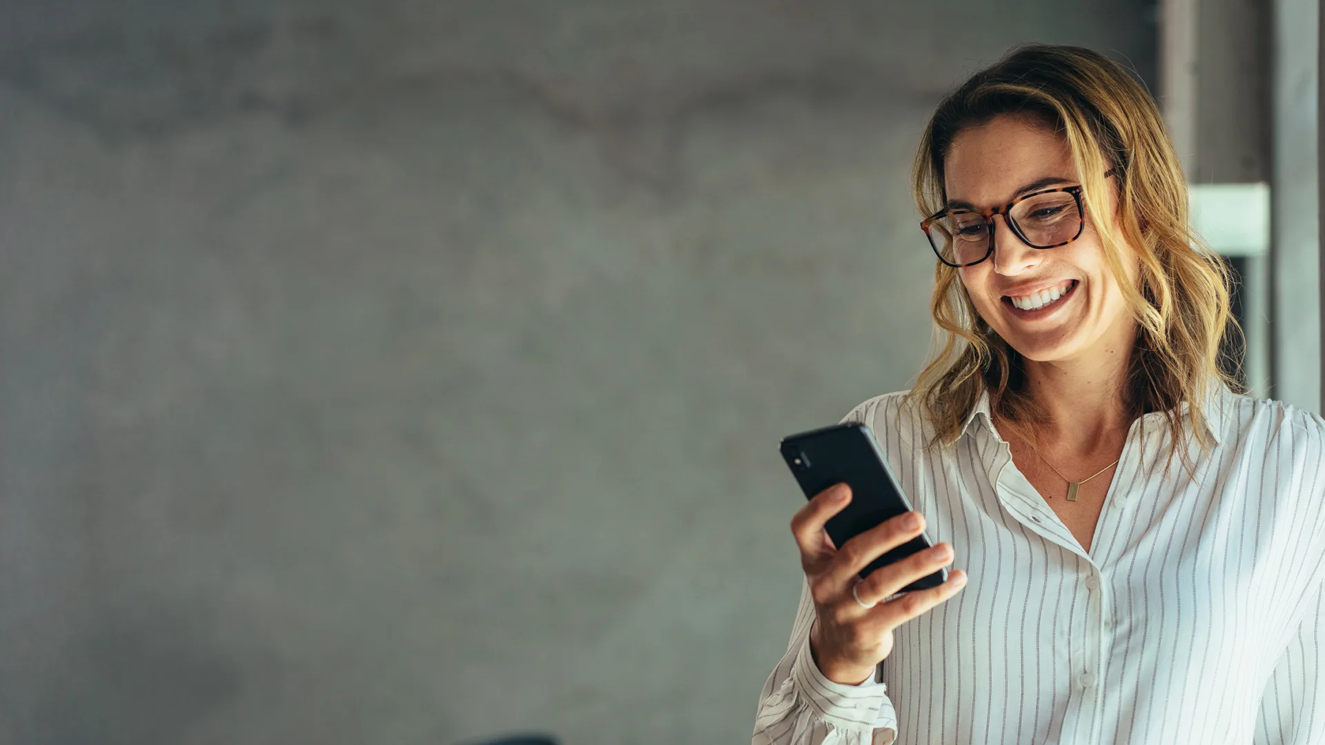 Smiling businesswoman using her phone in the office. Small business entrepreneur looking at her mobile phone and smiling while communicating with her office colleagues