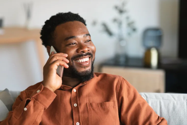 cheerful-black-guy-talking-cellphone-sitting-sofa-indoor