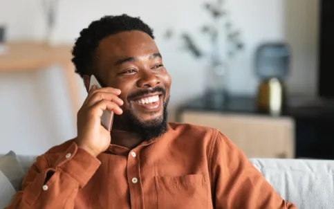 cheerful-black-guy-talking-cellphone-sitting-sofa-indoor