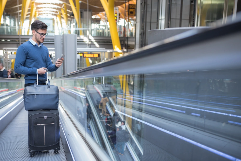 young-man-escalator-airport-using-his-mobile-phone-with-his-luggage-smiling.jpg